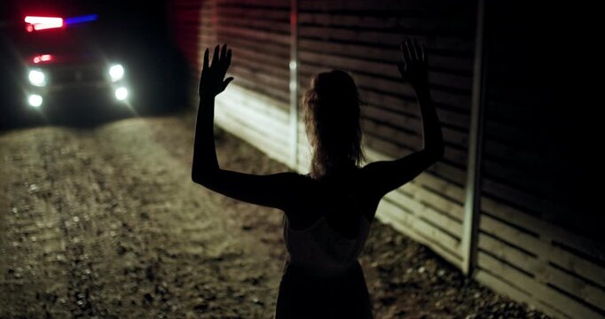 Girl stands with hands up in front of police vehicle at night in secluded area