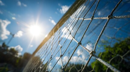 Close-up view of a soccer net against a bright sunny sky with clouds and sunlight.