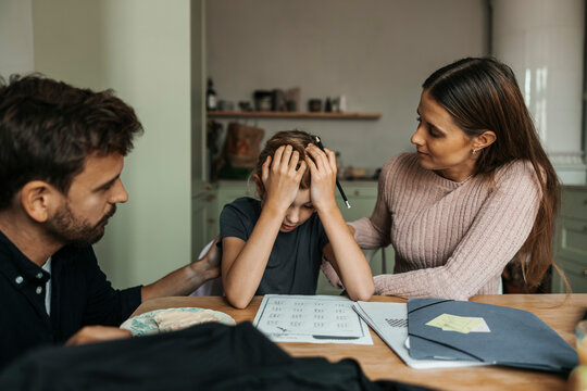 Parents consoling daughter stressing over studies while doing homework at home