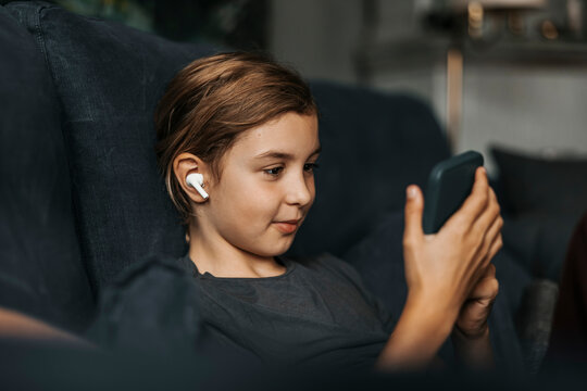 Girl wearing wireless in-ear headphones while using smart phone at home