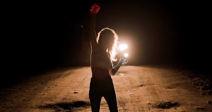 Girl dances in silhouette against the backdrop of car headlights on a dark road at night, creating a captivating visual experience filled with energy and movement
