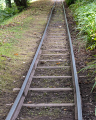 Fototapeta premium Old railway tracks lead through a green landscape toward sunlight in a peaceful setting near a wooded area