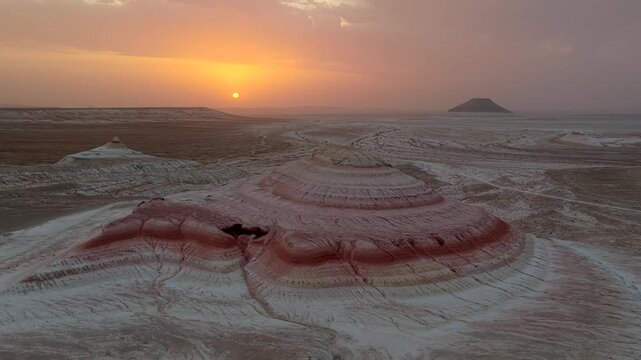 Aerial view of the terrain showcasing layered rock formations under the warm hues of the setting sun, Kyzyl Kup Tiramisu, Mangystau Region, Kazakhstan.
