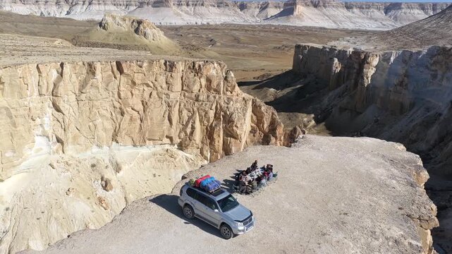 Aerial view of people gathered near a vehicle at Bozhira, with sandstone cliffs casting shadows on the arid landscape, Bozhira, Mangystau Region, Kazakhstan.
