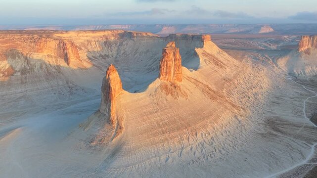 Aerial view of the majestic Bozhira Plateau, with its stark white terrain contrasting against the warm hues of the towering rock formations, Bozhira, Mangystau Region, Kazakhstan.