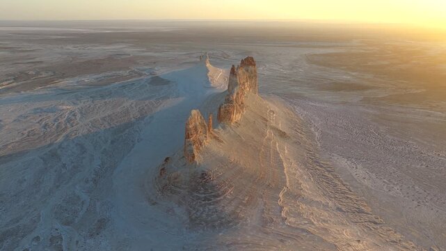 Aerial view of towering rock formations casting long shadows in the Bozhira landscape, contrasting against the vast, arid terrain, Bozhira, Mangystau Region, Kazakhstan.