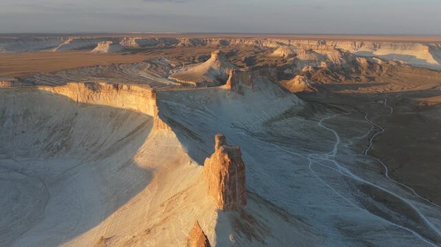 Aerial view of the sunlit Bozhira rock formations casting long shadows across the stark, pale landscape, creating a dramatic contrast, Bozhira, Mangystau Region, Kazakhstan.