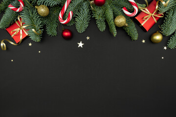 Evergreen Fir Branches with Red Gift Boxes, Christmas Ornaments and Candy Canes on Dark Background with Copy Space