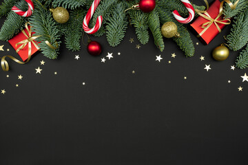 Evergreen Fir Branches with Red Gift Boxes, Christmas Ornaments and Candy Canes on Dark Background with Copy Space