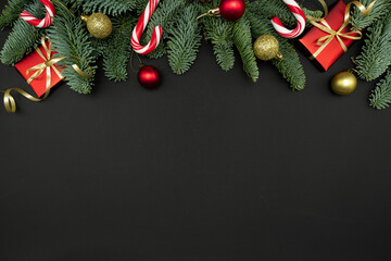 Evergreen Fir Branches with Red Gift Boxes, Christmas Ornaments and Candy Canes on Dark Background with Copy Space