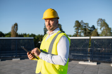 Worker inspecting rooftop solar panels holding digital tablet in hands