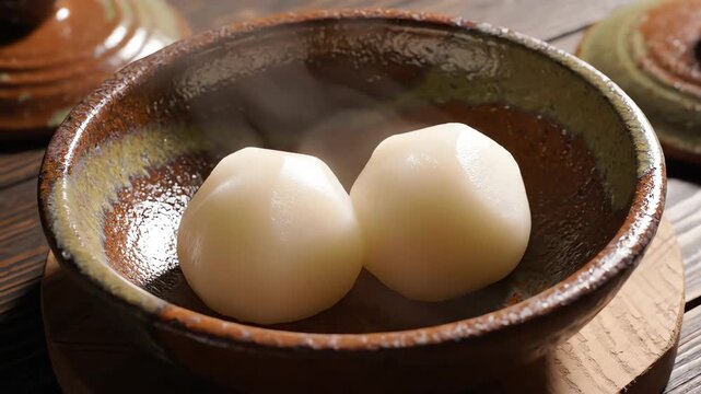 High angle overhead shot capturing two perfectly molded, smooth white pounded yam balls presented symmetrically in a deep rustic ceramic serving bowl symmetrically, rustic, bowl