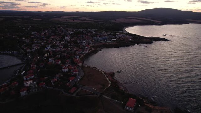 Aerial view of the Ahtopol coastline where the town's red-roofed buildings meet the dark blue sea under a dusky sky, Ahtopol, Burgas, Bulgaria.