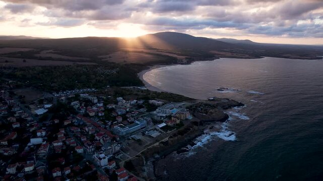 Aerial view of the beautiful coastline with buildings and ocean waves crashing against the rocks under a cloudy sky, Ahtopol, Burgas, Bulgaria.