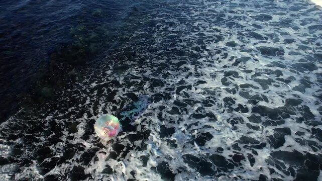Aerial view of the churning sea water with white foam contrasting against the deep blue, with a reflective inflatable ball, Ahtopol, Burgas, Bulgaria.