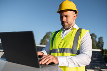 Man in safety vest analyzing data on laptop beside solar panels