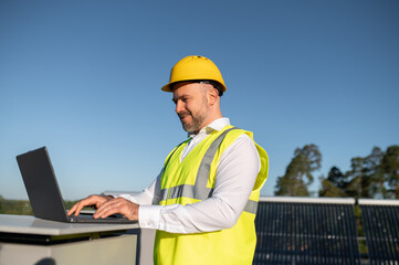 Man in safety vest analyzing data on laptop beside solar panels