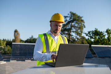 Engineer in helmet working on laptop near solar panels outdoors