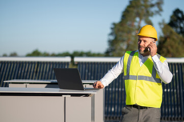 Engineer in helmet talking on phone near solar panels outdoors