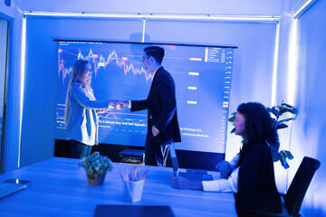 Business meeting between two professionals shaking hands in a modern office with financial data projection