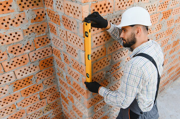 Construction worker using spirit level on brick wall