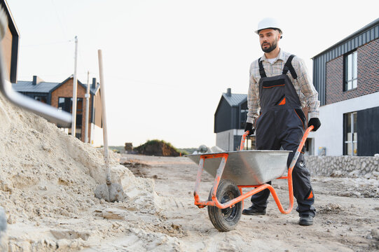 Construction worker moving sand with wheelbarrow on building site - Powered by Adobe