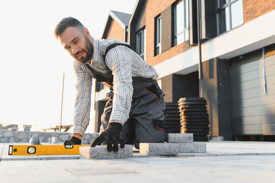 Worker leveling paving slabs on new house backyard