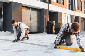 Construction workers installing paving stones using spirit level
