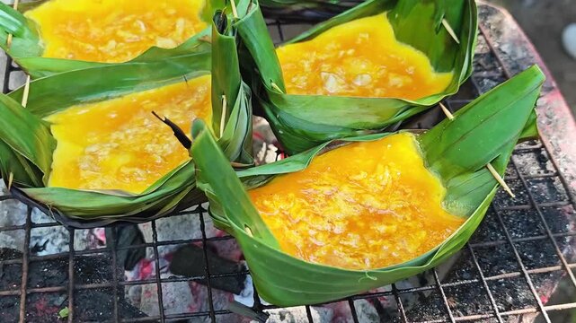 Khai Pam, a traditional Northern Thai savory dish made with eggs and seasoning sauce, cooked in banana leaf cups and grilled over a charcoal stove.
