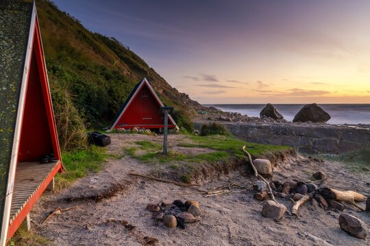 two small red wooden A-frame bothy and fireplace on the north coast of Bornholm island at sunset