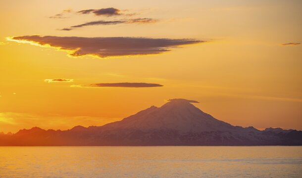 View of Cook Inlet on white mountain peaks of Mount Redoubt at sunset, picturesque golden light of the midnight sun, mountains of the Aleutian Range, Anchor Point, Anchor River State Recreation Area, Alaska, USA