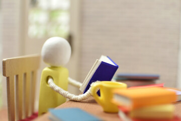 読書をする木製人形の写真　積まれた本　趣味の時間　勉強　ミニチュア