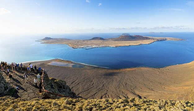 View of La Graciosa island with volcanic craters in the evening light, tourists on an observation deck at the Mirador del R&iacute;o viewpoint designed by artist C&eacute;sar Manrique, Lanzarote, Canary Islands, Spain