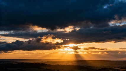 The first rays of sunlight break through dark clouds at dawn over a landscape. travel magazines, destination branding, designed for outdoor magazines and nature guides.