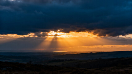 The first rays of sunlight break through dark clouds at dawn over a landscape. travel magazines, destination branding, designed for outdoor magazines and nature guides.
