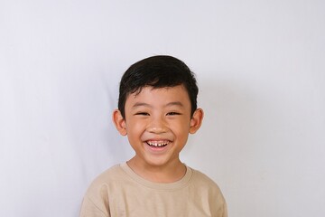 Happy Asian boy smiling naturally in a studio portrait with white background, ideal for childhood happiness and lifestyle concepts.