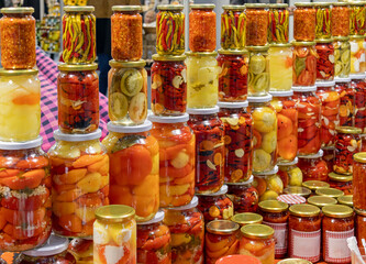 Homemade colorful pickled vegetables inside closed glass jars sold on market stall
