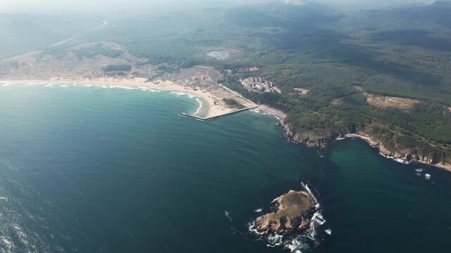 Aerial view of the beach with the dark blue sea meeting the sandy shore under a blanket of sky, contrasting with the green forest, Arkutino, Primorsko, Bulgaria.
