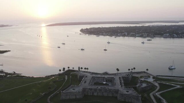 Aerial view of the ancient Castillo de San Marcos fortress, seen against a tranquil bay dotted with sailboats at sunset, St. Augustine, Florida, United States.