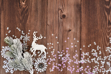 Snow-covered fir branch and deer on the background of a dark wooden table with snowflakes. Christmas or New Year greeting card.