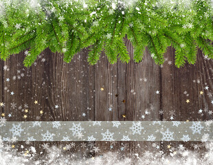 Christmas or New Year greeting card. Branches of spruce and ribbon with snowflakes and golden stars on snowbound wooden background.