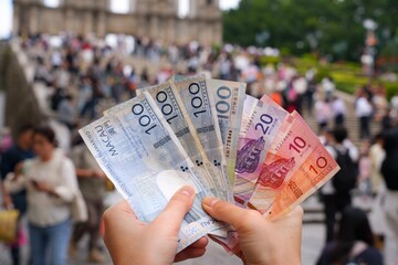 Makau pataca money. Currency of Macau - hand holding used banknotes. City in background.