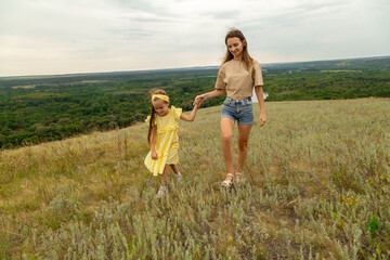 Mother and daughter as they walk through the field, having fun and laughing in summer day