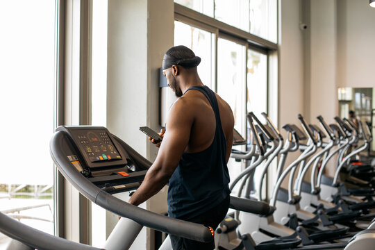 A man on a treadmill in the gym. A man in sportswear uses a mobile phone while walking on a treadmill in a modern gym.