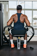 Strong athlete using strength machine in gym. Rear view of a muscular athletic man training back...