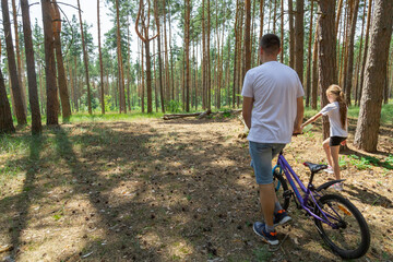 Obraz premium father and daughter walking with a bicycle in the forest