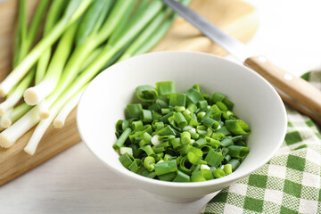 Cut green onions in bowl on white wooden table, closeup