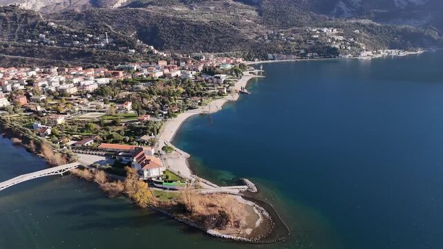 Aerial view of Lago di Garda's tranquil waters meeting the shoreline's sandy beach, contrasting with the town's buildings, Torbole, Trentino-Alto Adige, Italy.