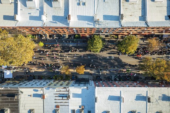 Aerial view of people gathering in a street lined with rooftops and trees casting long shadows, creating a vibrant scene, Brooklyn, New York, United States.