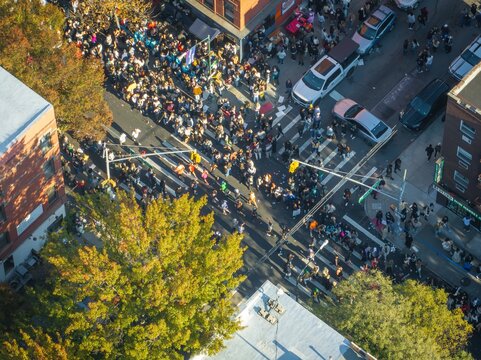 Aerial view of a bustling crowd crossing streets near brick buildings, the scene filled with cars and the vibrant colors of autumn foliage, Brooklyn, New York, United States.